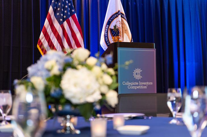 The stage podium at the Collegiate Inventors Competition, viewed from behind the flowers sitting on top of a banquet table