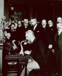 Bell talking on a telephone in front of a crowd of onlookers