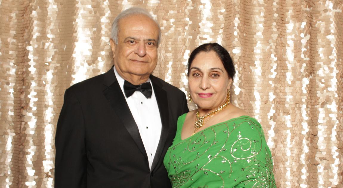 Asad Madni and his wife pose in front of a sparkling gold photo backdrop